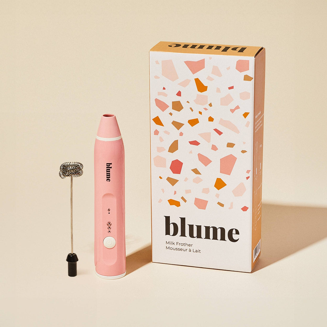 Pink milk frother with terrazzo patterned packaging on a beige background