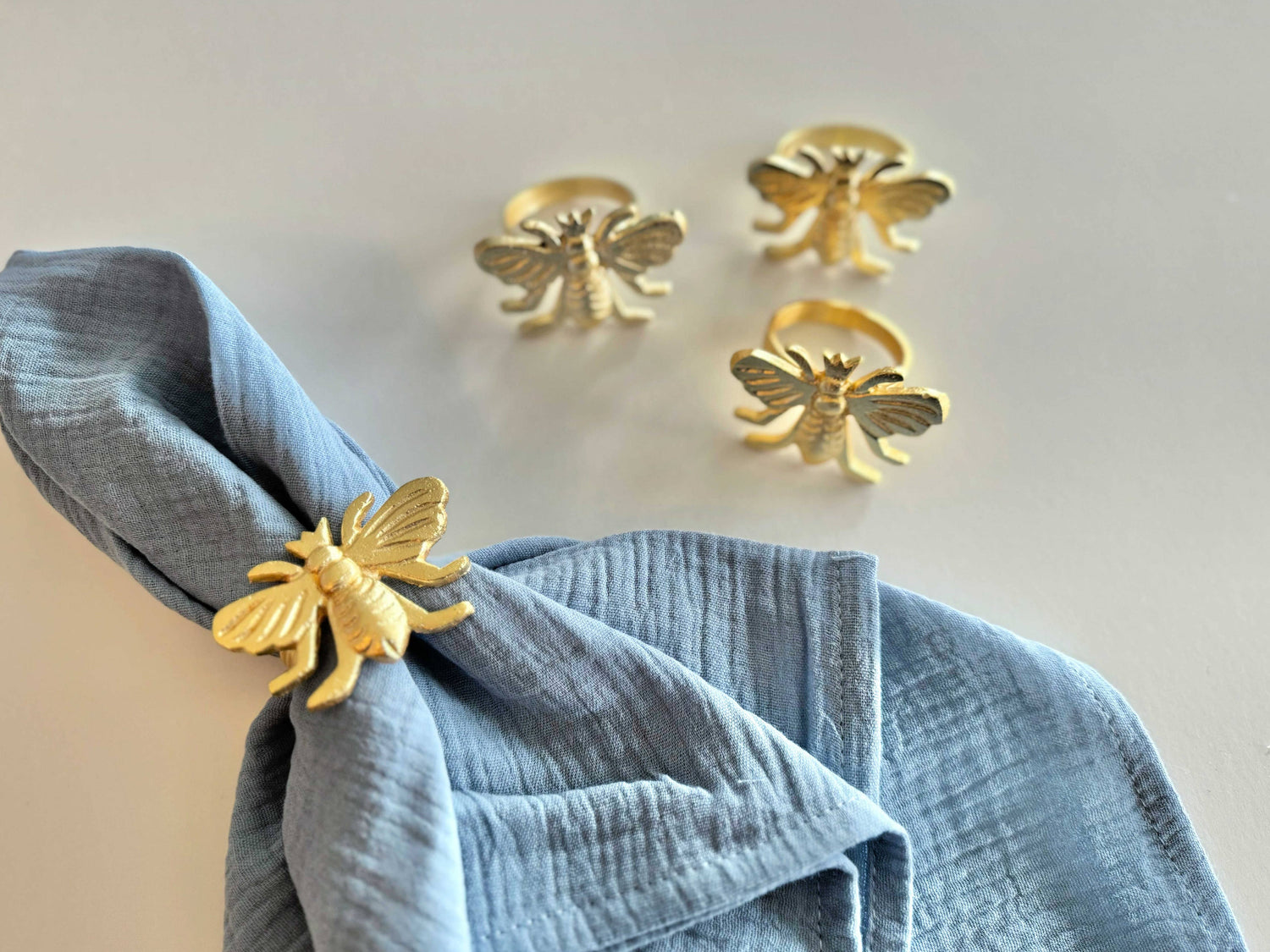 Gold bee-shaped napkin rings on a blue napkin against a light background