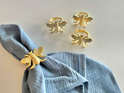 Gold bee-shaped napkin rings on a blue napkin against a light background