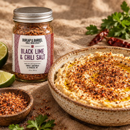 A bowl of hummus sprinkled with black lime and chili salt with a jar of the spice next to it