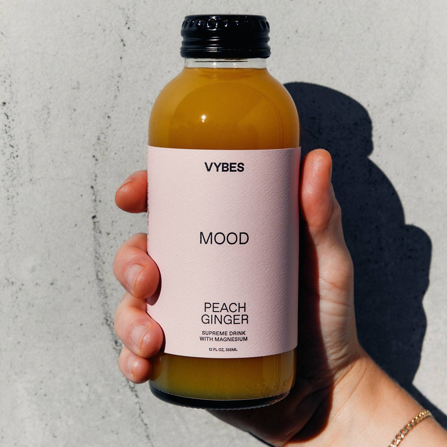 Hand holding a bottle of VYBES Mood Peach Ginger juice against a gray background