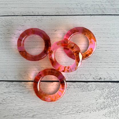 Set of four pink and orange translucent rings on a light wooden surface