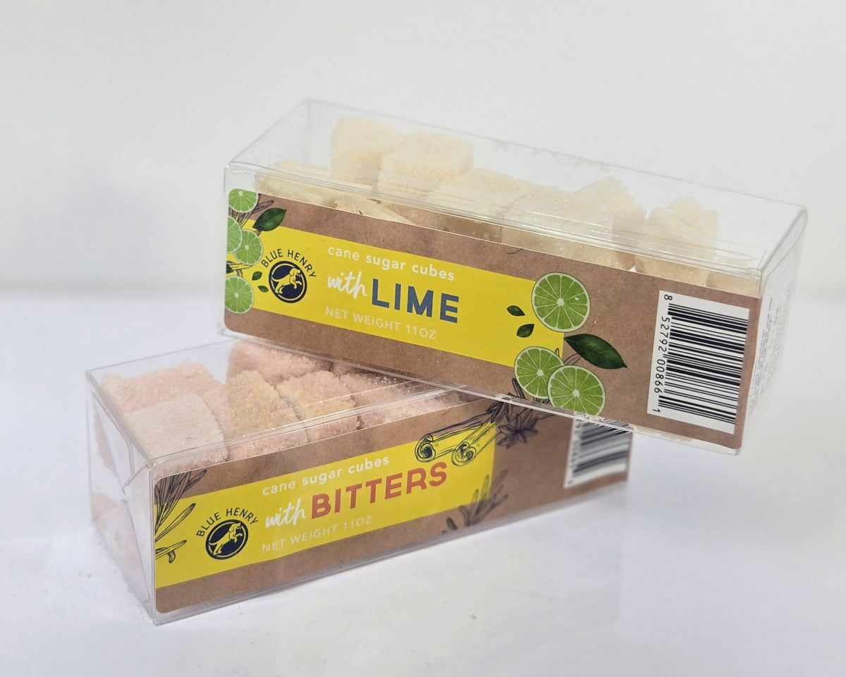 Two clear plastic boxes of cane sugar cubes on a white background. One with lime and another with bitters.