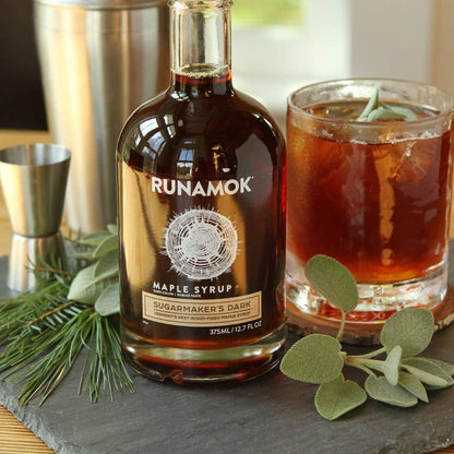 Bottle of Runamok Maple Syrup with a glass of a drink on a slate surface.