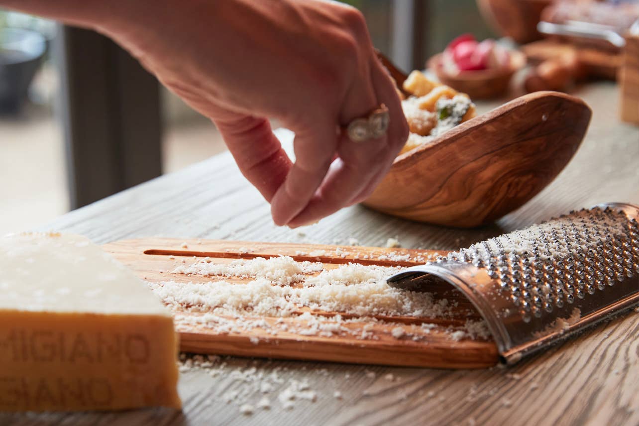 Person grating cheese with a wooden grater on a table.