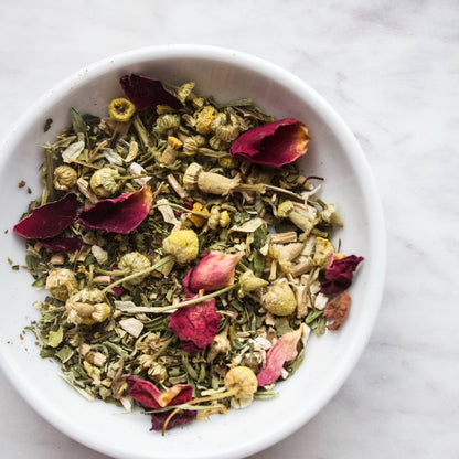 White bowl filled with dried herbs and flowers on a marble surface