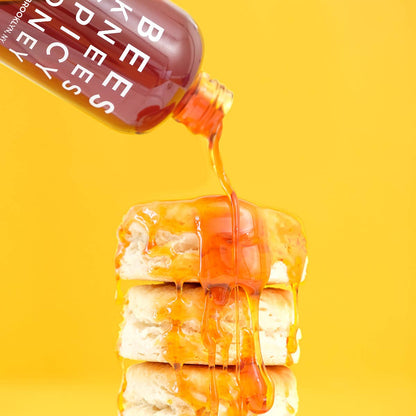 Honey being poured from a bottle onto a stack of pancakes on a yellow background