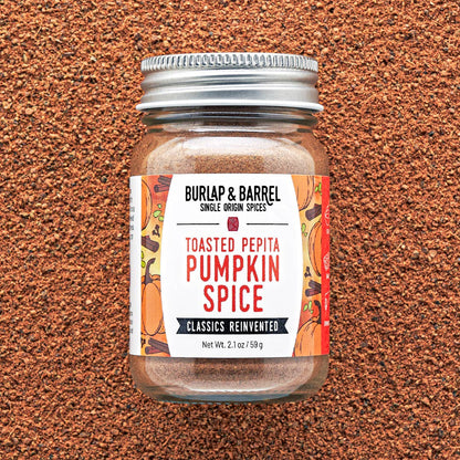 A jar of Burlap &amp; Barrel Toasted Pepita Pumpkin Spice centered on a textured brown background. 
