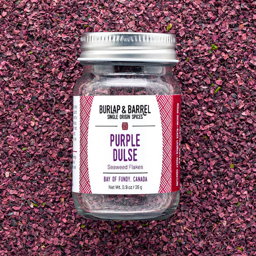 Jar of Burlap & Barrel Purple Dulse flakes on a pinkish-purple textured background