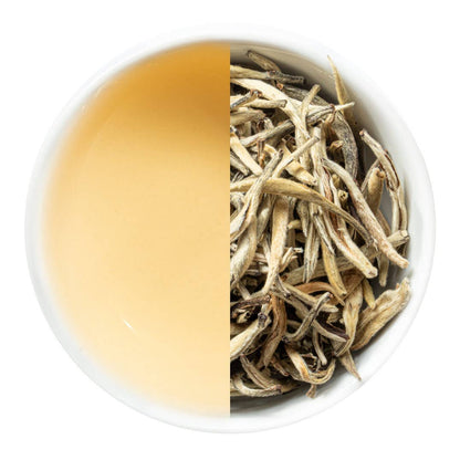 Silver Needle Tea leaves and brewed tea in a white cup on a white background