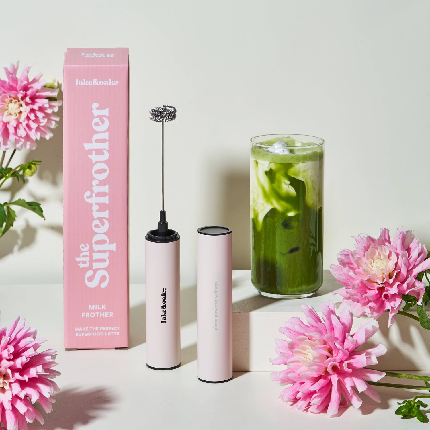 Pink milk frother with packaging and flowers on a light background