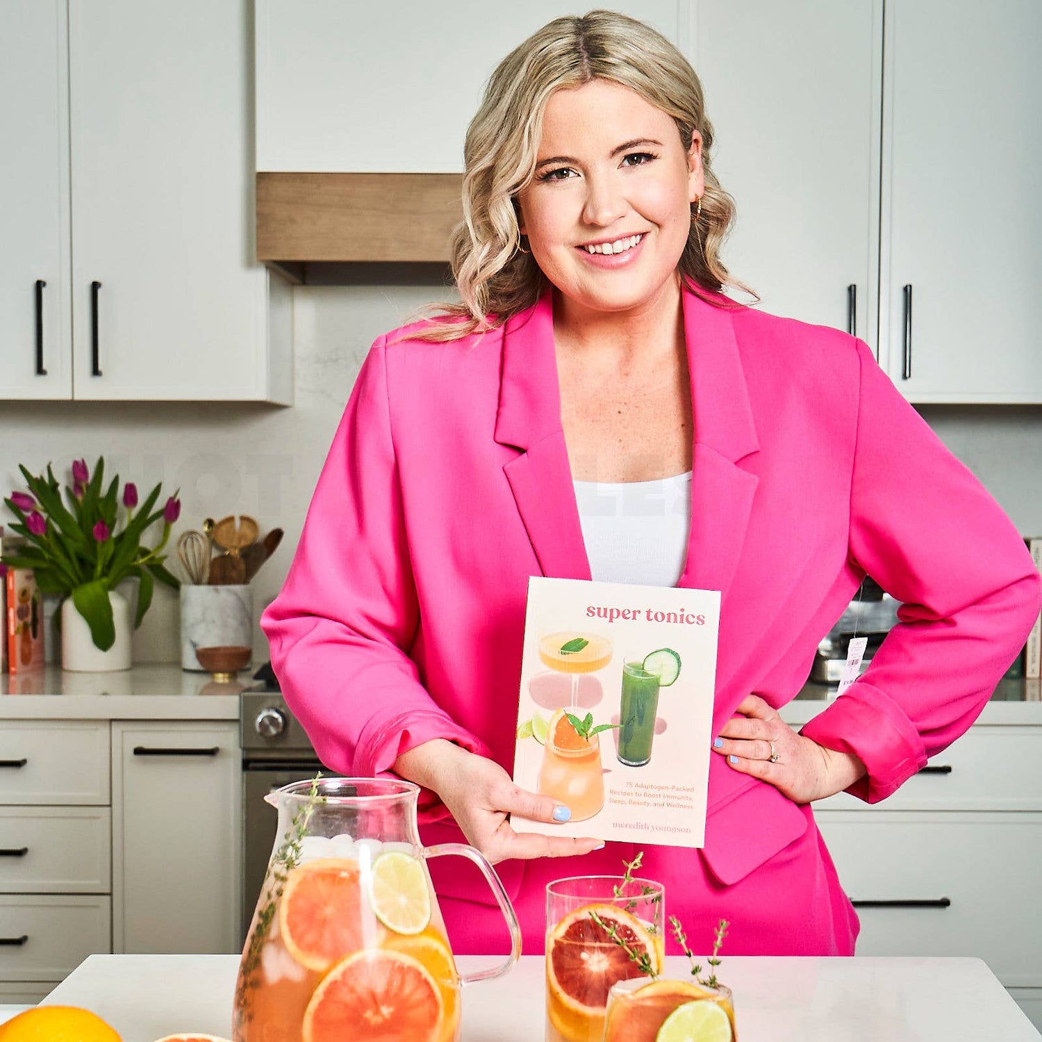 Woman in a kitchen holding a book with drinks on a counter