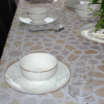 Dining table setting with white ceramic bowls and plates on a patterned tablecloth.