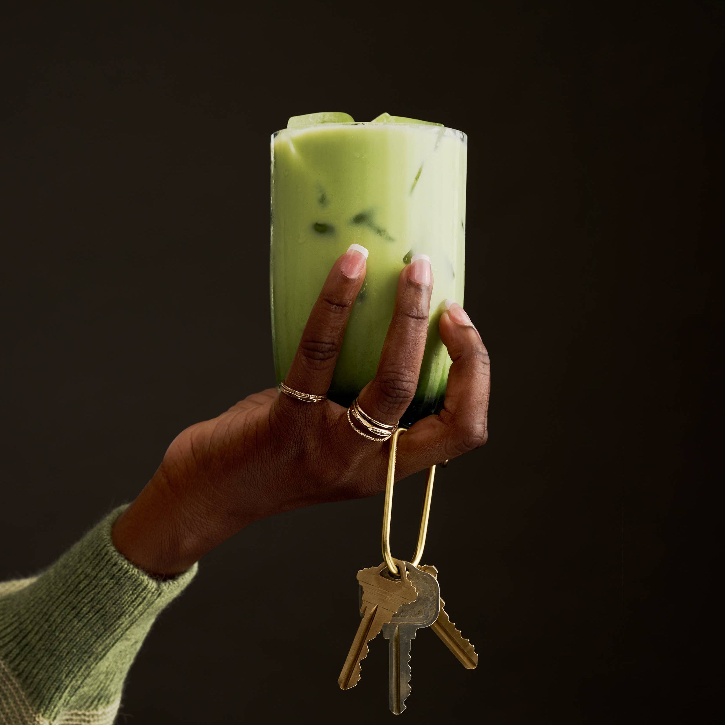 Hand holding a green cylindrical container with keys attached, against a black background